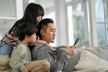 young asian father and two kids looking at cellphone together
