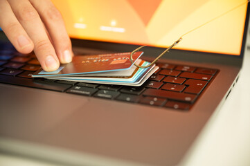 Visualisation of a person trying to prevent phishing and online fraud by holding a leaked credit card on a PC keyboard that is hanging on a fishhook