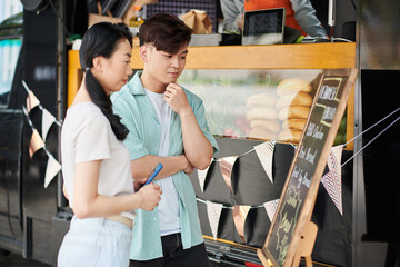 Pensive young people looking at food truck menu deciding what to order