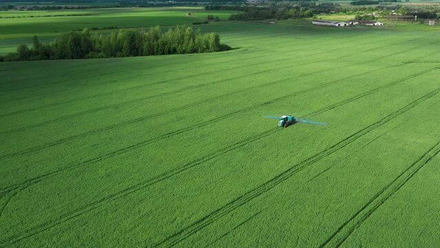 Agricultural machinery spraying fertilizers chemicals on green field of corn soybeans cereal rapeseed, spring work. Agronomist on tractor spraying herbicides and pesticides on rural field. Aerial view