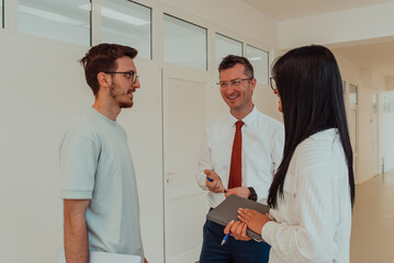 Obraz premium The director conducts a conversation with the secretary and a young programmer in a modern and spacious corridor of a large company, discussing various business topics and projects.