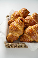 Fresh croissants in a basket, isolated on white background.