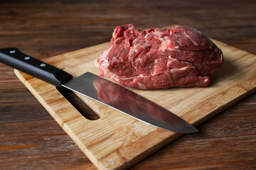 A piece of fresh beef and a knife on a cutting board. Room for text. High quality photo
