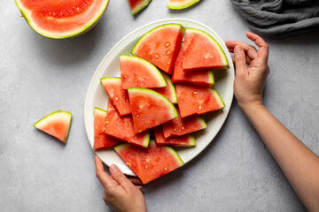 Female hands holding a plate with fresh juicy watermelon slices.