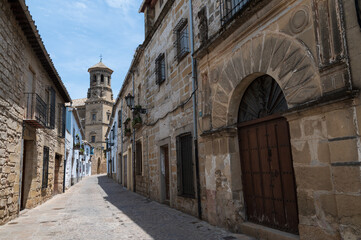 Vista de una antiigua casa con arco en una calle típica de Baeza, Jaén, Andalucia, españa con una torre de iglesia al fondo. - obrazy, fototapety, plakaty