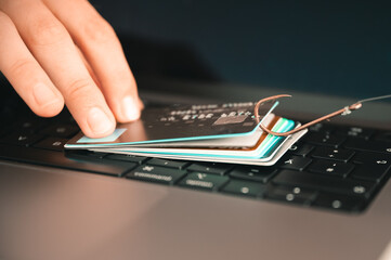 Visualisation of a person trying to prevent phishing and online fraud by holding a leaked credit card on a PC keyboard that is hanging on a fishhook
