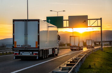 Rear angle view of delivery cargo trucks on the road going to the west with sunset in the background. Fast delivery, cargo logistic and freight shipping concept