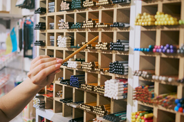 Close-up emale hand takes out a graphite pencil from a display in school stationery shop. Seller performs merchandising