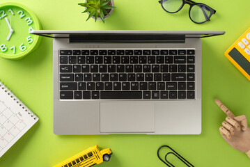 Engage in distant learning with this top-view shot, showcasing a laptop, calendar, clock, glasses and school supplies like calculator, paper clips on isolated light green background