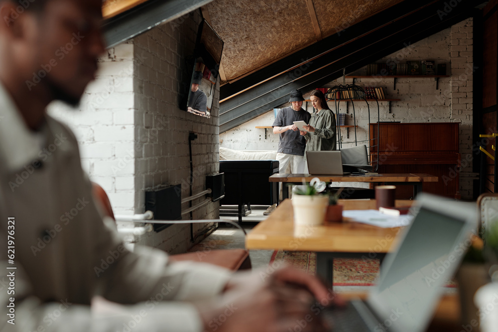 Poster focus on two young analysts or managers looking at screen of tablet held by brunette woman and discu