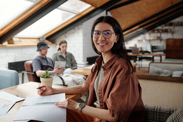Happy young Asian female chief executive officer in eyeglasses looking at camera with smile while...