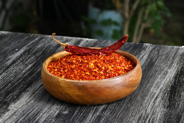 Wooden bowl with crushed chili pepper and fresh red chili pepper on old table. Selective focus.