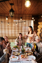 Thanksgiving Day, Family of five and dog Yorkshire terrier during family dinner outdoors at sunset table eating and drinking, having fun, singing songs with guitar