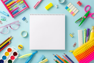 Education for small kids concept. Top view photo of empty notepad page offering copy-space, glasses, pencil case and other colorful school supplies on isolated pastel blue background
