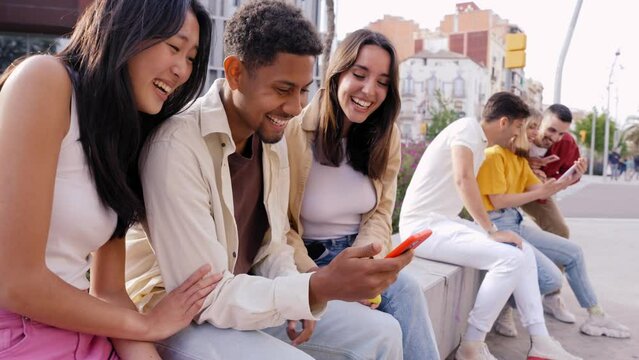 Multiracial happy group of friends using phone and smiling together outdoor. People addicted to technology and social media. Fun young and networks as means of communication.