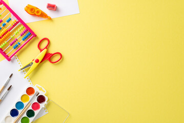 Get inspired by the world of education with this captivating top-down image: an album pages, watercolor paints, abacus and vibrant stationery on a yellow backdrop, perfect for advertising or text