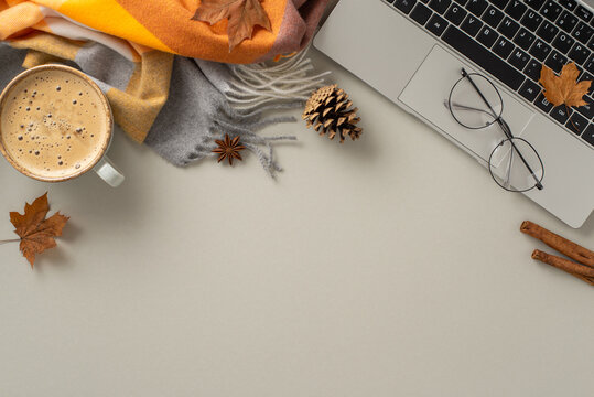 A top view image encapsulates the essence of working from home, showcasing a laptop with a cozy blanket, pinecones, spices, glasses and a cup of coffee on grey isolated backdrop, offers copyspace