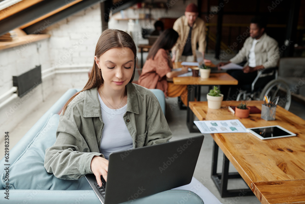 Aufkleber Young female analyst in casualwear networking while sitting on comfortable blue couch in front of camera against colleagues