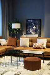 Two soft brown couches with cushions making corner in spacious room or coworking area with round table, bench and ottoman standing on carpet