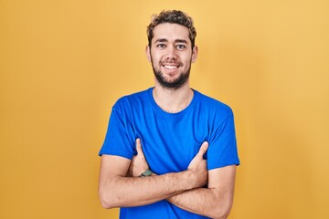 Hispanic man with beard standing over yellow background happy face smiling with crossed arms looking at the camera. positive person.