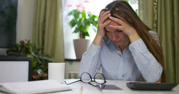 Woman sit at desk with paper bills, feeling stressed about bank loan payments