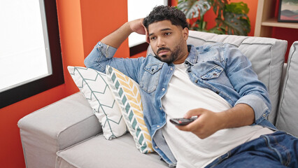 African american man watching tv lying on sofa with boring expression at home