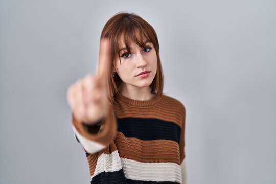 Young beautiful woman wearing striped sweater over isolated background pointing with finger up and angry expression, showing no gesture