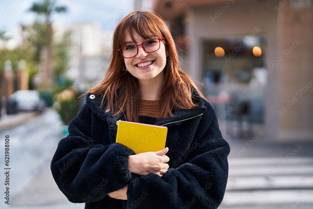 Sticker Young woman smiling confident hugging book at street