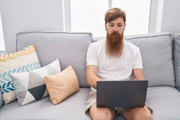 Young redhead man using touchpad sitting on sofa at home