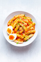Tteokbokki with eggs, fresh green leek and roasted sesame seeds on the white table top. Tteok-bokki is a Korean cuisine dish with rice gnocchi sticks and spacy sauce. Asian food, fast Korean food