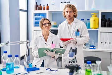 Fototapeta premium Two people working at scientist laboratory smiling looking to the side and staring away thinking.