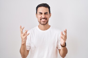 Fototapeta premium Handsome hispanic man standing over white background crazy and mad shouting and yelling with aggressive expression and arms raised. frustration concept.