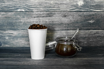 a paper cup with coffee beans next to a glass jar with ground coffee on a dark background