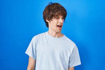 Fototapeta premium Hispanic young man standing over blue background winking looking at the camera with sexy expression, cheerful and happy face.