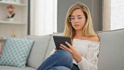 Young blonde woman wearing glasses using touchpad at home