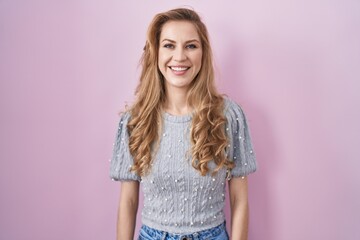 Beautiful blonde woman standing over pink background with a happy and cool smile on face. lucky person.