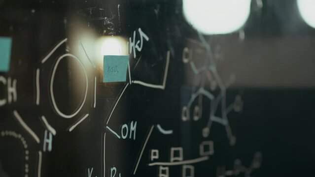 Writing on the board, a middle-aged doctor confidently glues a sticker, fastens a note In a scientific laboratory. Professional worker Developing a vaccine Studying research data, experiments
