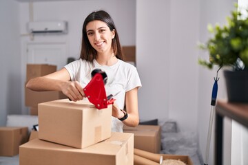 Young beautiful hispanic woman smiling confident packing cardboard box at new home