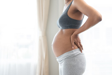 African American pregnant woman standing near the window in bedroom at home. motherhood, pregnancy, and expectation concept.