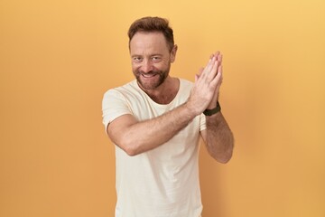 Middle age man with beard standing over yellow background clapping and applauding happy and joyful, smiling proud hands together