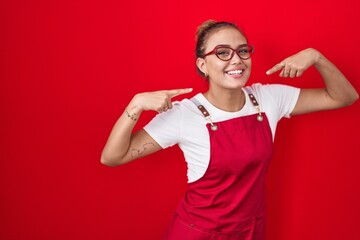 Young hispanic woman wearing waitress apron over red background smiling cheerful showing and...
