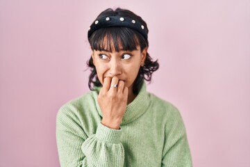 Young beautiful woman standing over pink background looking stressed and nervous with hands on mouth biting nails. anxiety problem.