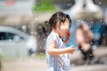 広場の噴水で水遊びしている3歳の女の子