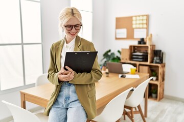 Young blonde woman business worker smiling confident holding clipboard at office