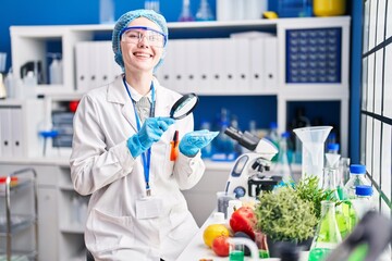 Young blonde woman scientist looking sample with magnifying glass at laboratory