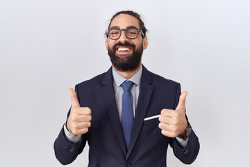 Hispanic man with beard wearing suit and tie success sign doing positive gesture with hand, thumbs up smiling and happy. cheerful expression and winner gesture.