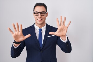 Young hispanic man wearing suit and tie showing and pointing up with fingers number ten while smiling confident and happy.