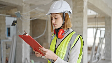 Young blonde woman architect reading document at construction site