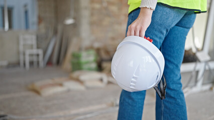 Young blonde woman builder holding hardhat walking at construction site