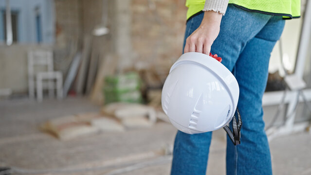 Young blonde woman builder holding hardhat walking at construction site